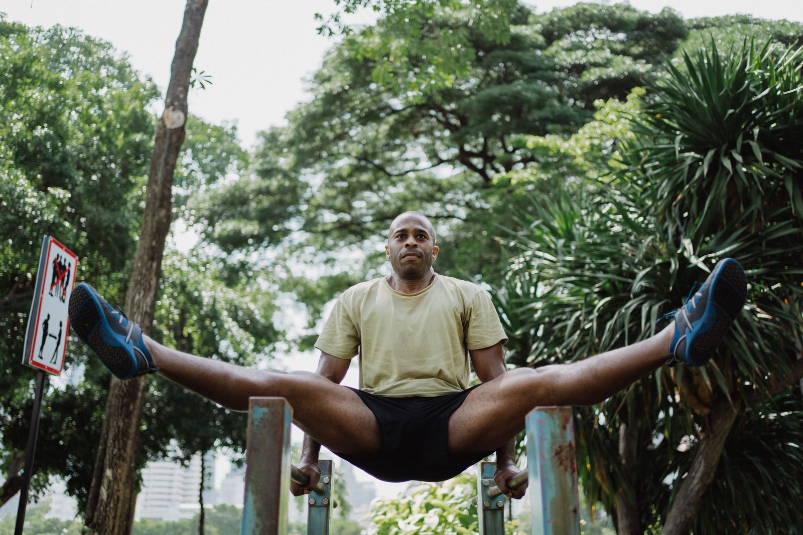 A man holding a straddle position on outdoor parallel bars in a green park
